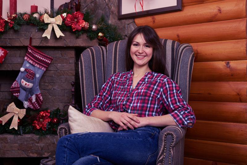 圣诞节装饰品旁坐在扶手沙发椅上微笑的美女