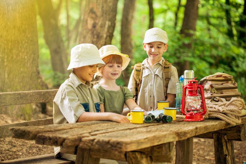 森林里阳光下坐在老旧木桌上研究地图的探险的孩子们