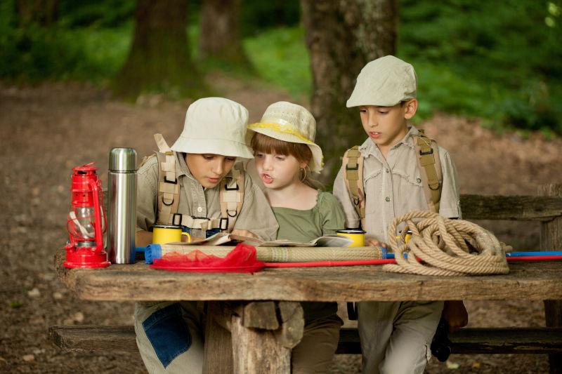森林里’坐在木桌旁研究地图的探险的孩子们