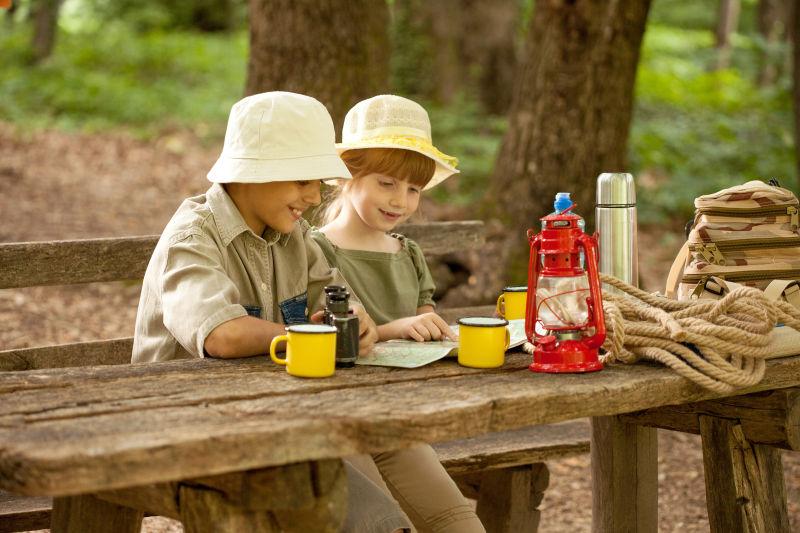 坐在木桌旁研究地图的野外探险的孩子们