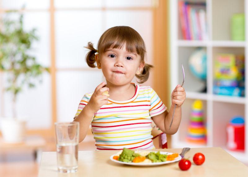 餐桌边在吃蔬菜的小女孩