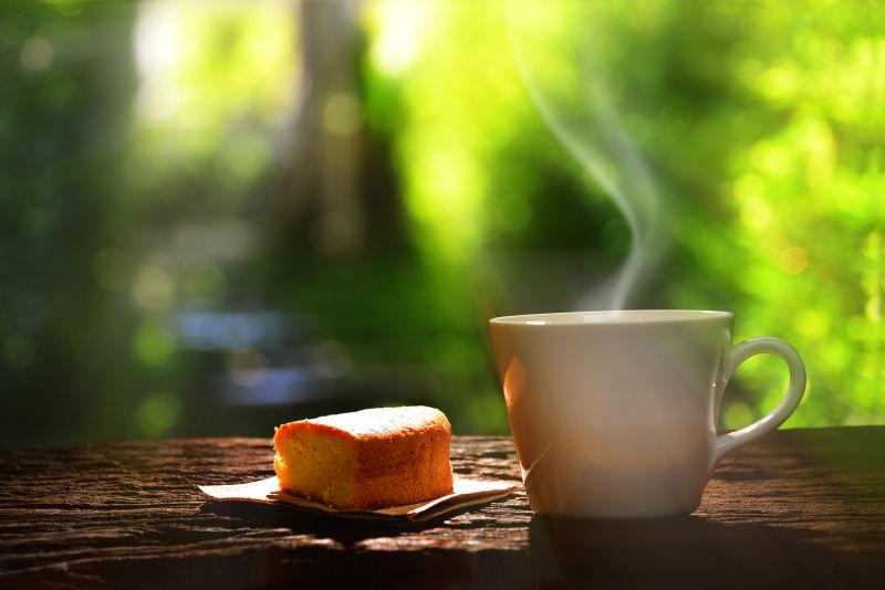 绿色背景下的木桌上的一块面包和一杯热咖啡
