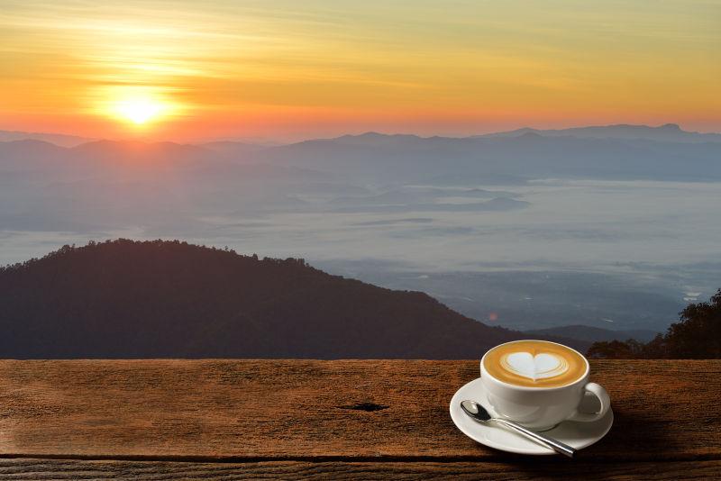 日出背景下的木桌上的一杯热咖啡