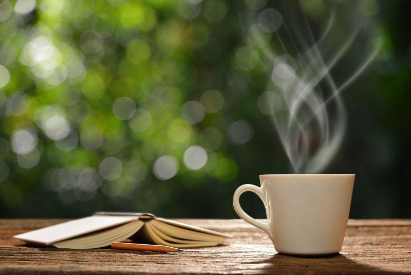 绿色户外背景下的木桌上的一杯咖啡和一本书