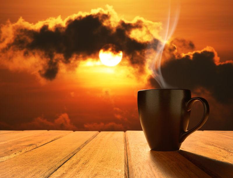 云后的日出背景下的木桌上的一杯热咖啡