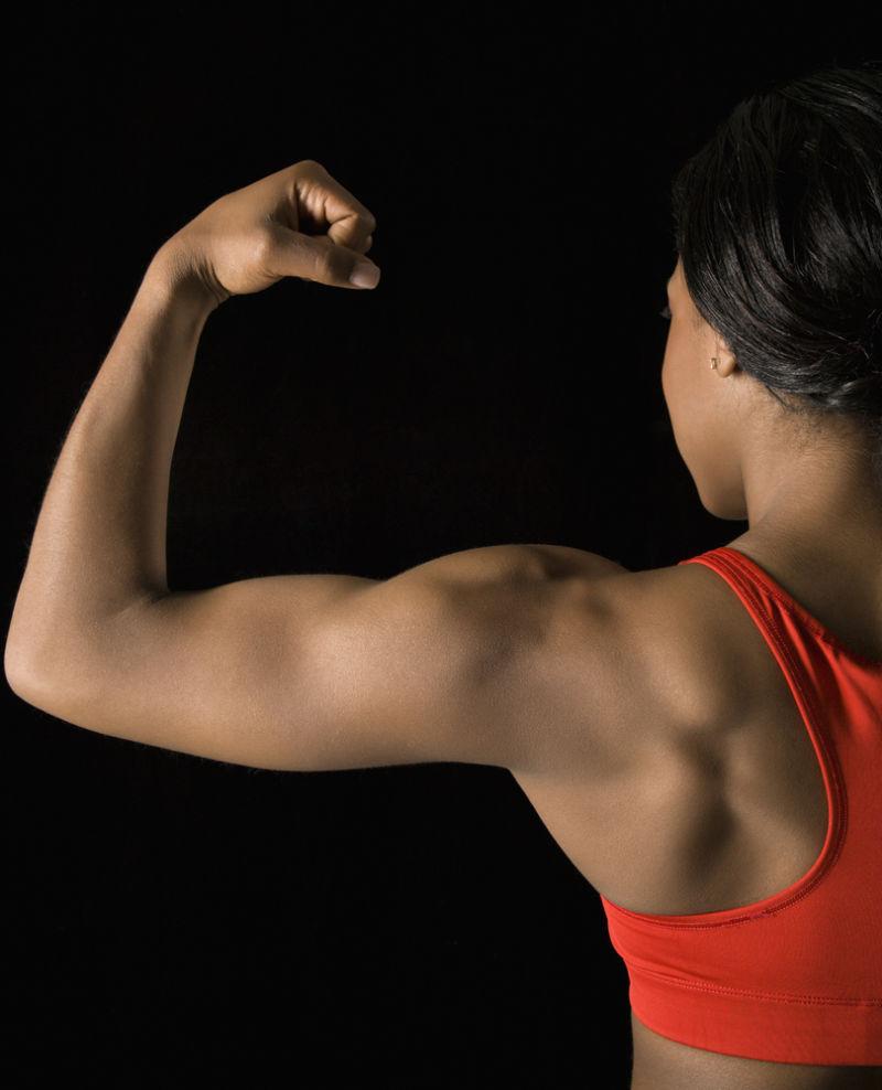 在黑色背景下非洲裔美国妇女弯曲肌肉二头肌的后视图