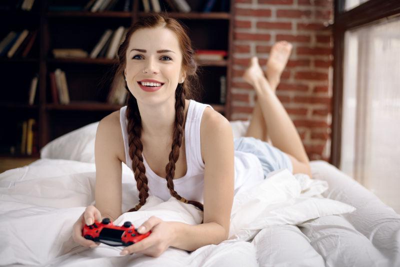 女孩在家里的床上玩游戏机