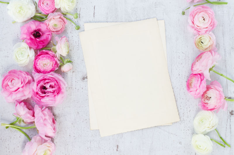 白色木板上的粉色毛茛花和空白纸张