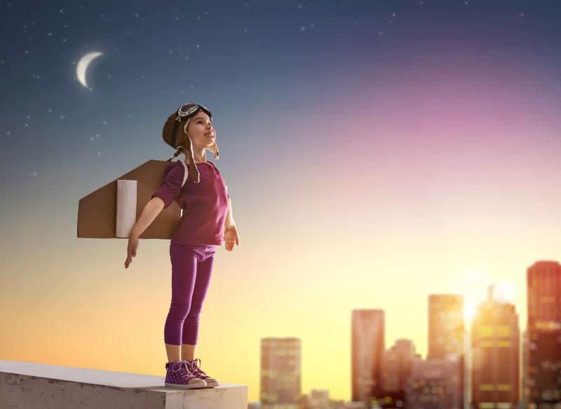 日出-日落的城市背景下的背着玩具飞机站在高处的小女孩