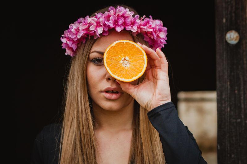带着花卉头饰的女人拿着半个橙子