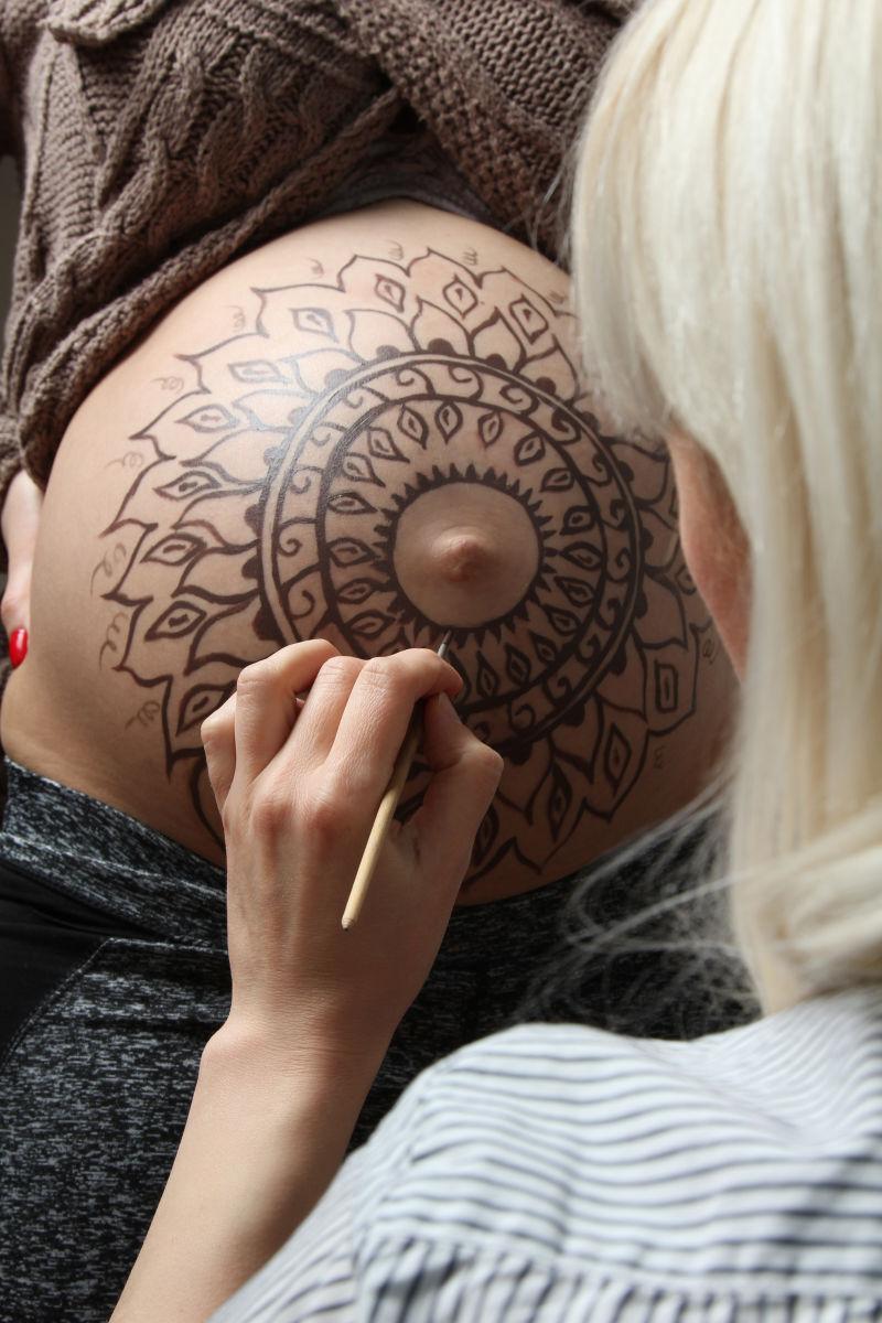 纹身师在为孕妇肚子上画纹身