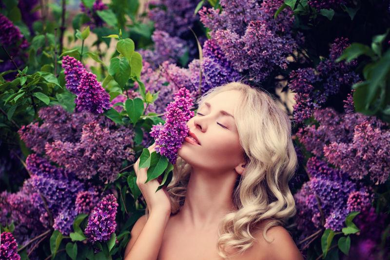 金发女人在花园里享受着紫色丁香花的气息