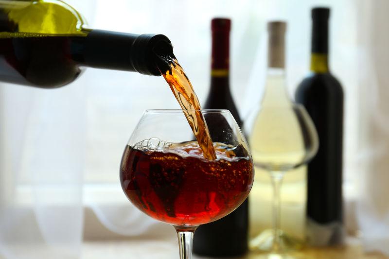 不同品种的酒瓶背景下倒入高脚杯内的红酒