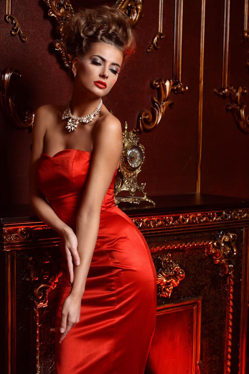 穿着红色抹胸长尾礼服倚靠在红色柜子上的美女