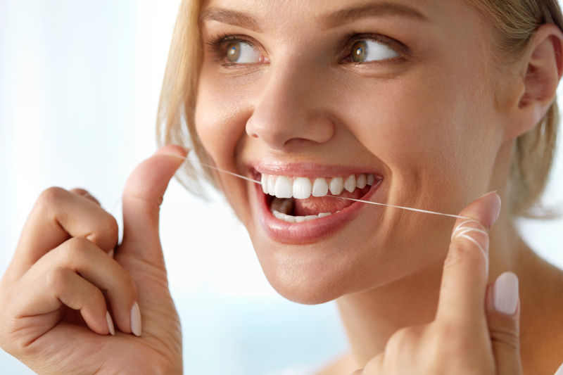 微笑的女人用牙线清洁牙齿