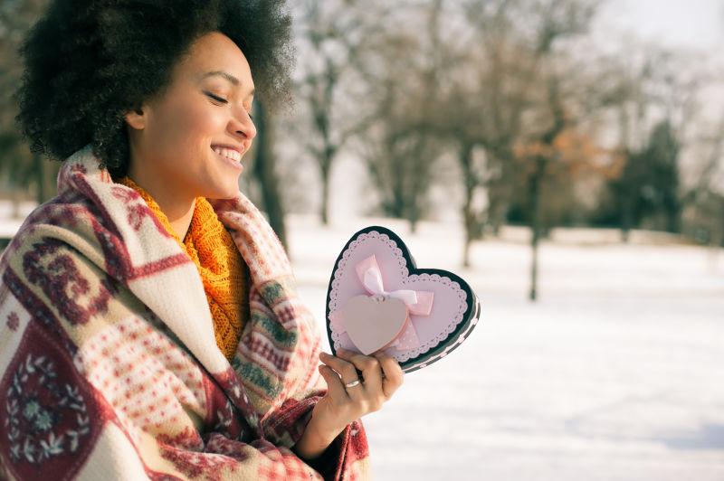 快乐的年轻微笑的女人在冬天拿着心形卡片