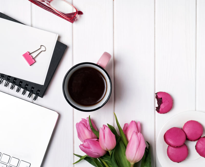 白色办公桌上的一杯咖啡粉色郁金香与笔记本