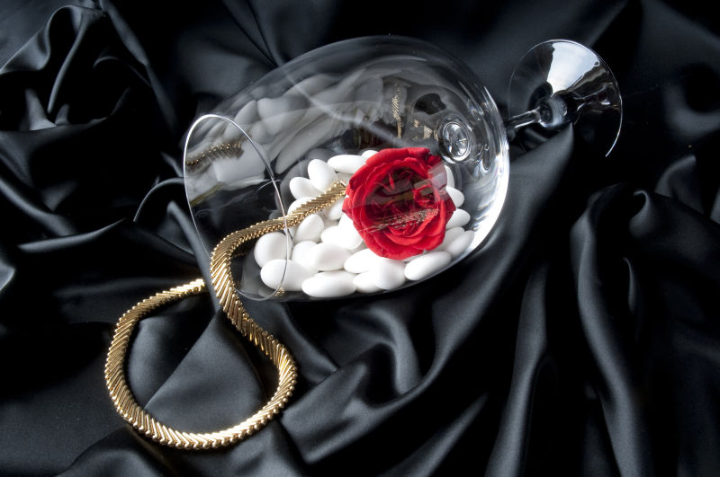 黑色背景中的高脚杯红玫瑰和项链