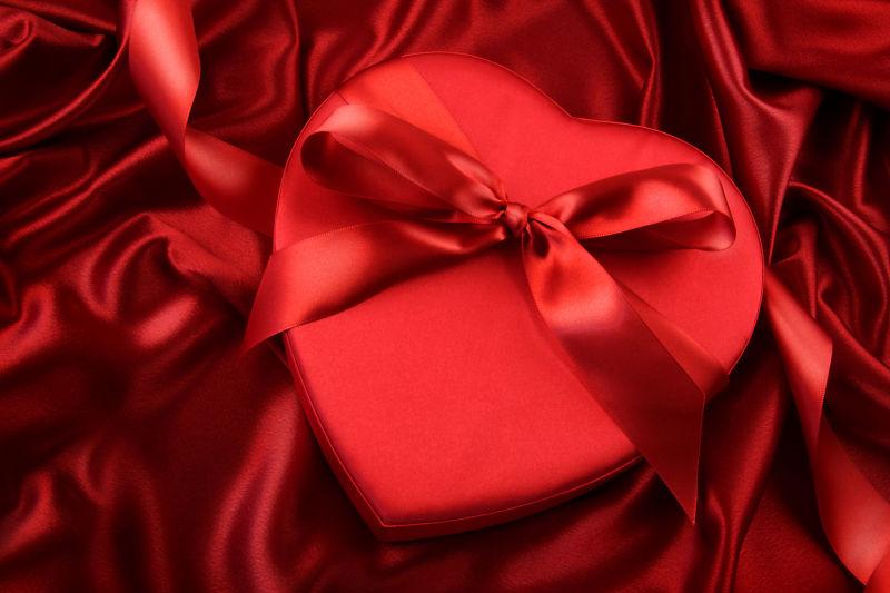红色丝绸背景中的心形礼物盒