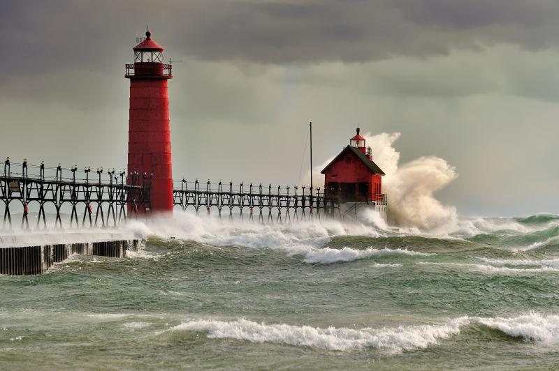 灰色天空下红色灯塔旁边的海浪
