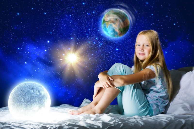 太阳系星空背景前坐在床上的小女孩
