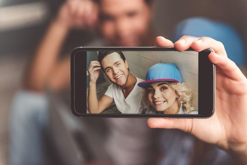 使用智能手机自拍戴帽子的时髦年轻夫妇