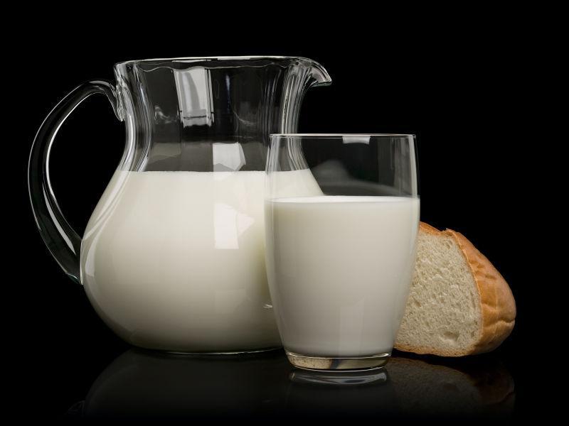 黑色背景一块白面包和装满牛奶玻璃杯