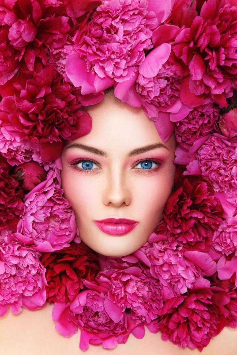 粉红色牡丹花覆盖的年轻的蓝眼美女