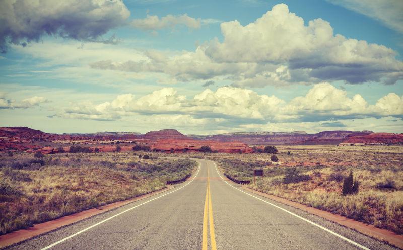 蓝天白云下的黄色的山中的老式风格的沙漠公路
