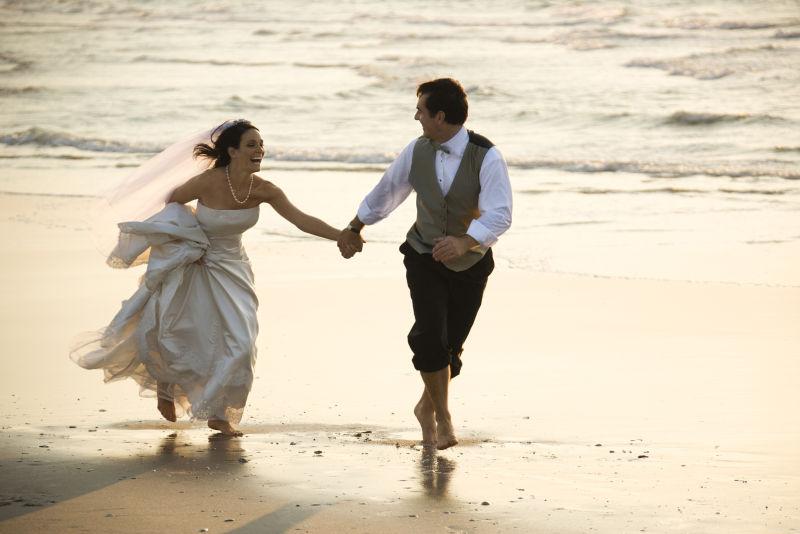 新郎和新娘赤脚跑在海滩上