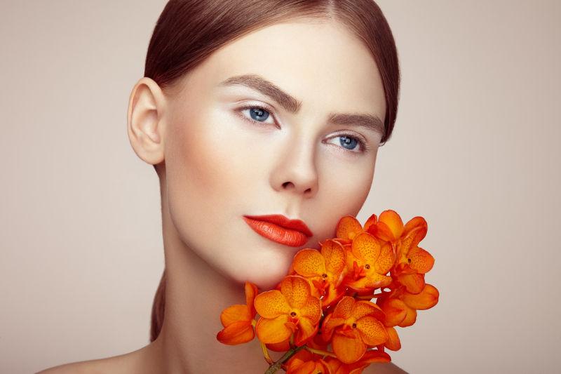 化妆的美女拿着橙色兰花