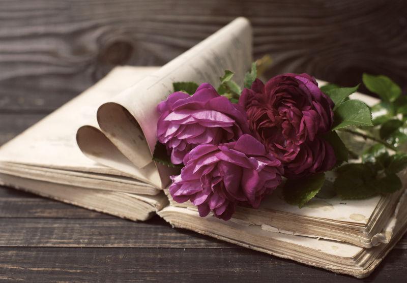 木制桌面上的紫色牡丹和书