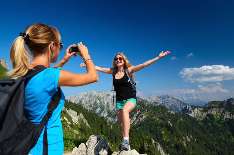 背着背包的年轻女士在阿尔卑斯山帮同伴拍照