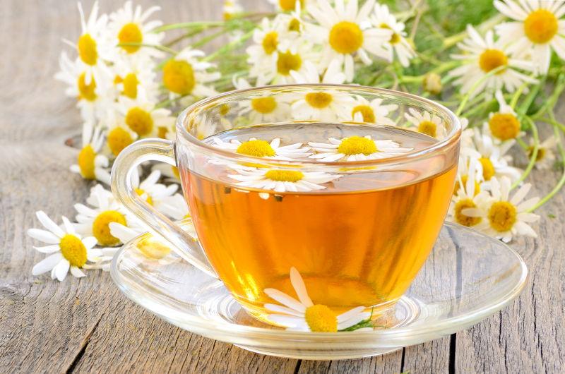 放在木桌上的透明茶杯里黄色的茶和一束花