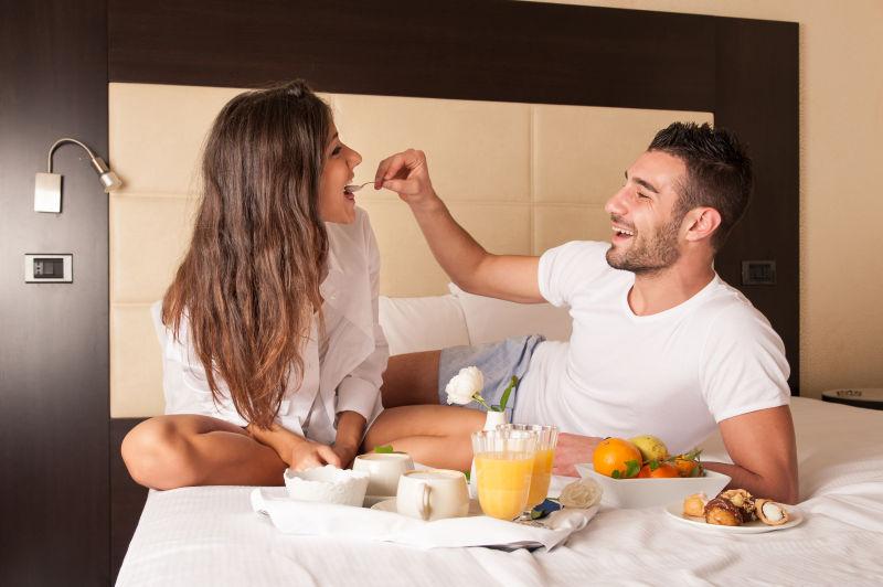年轻幸福的夫妇在床上吃早餐