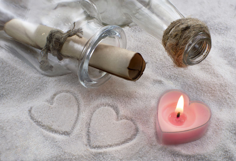 沙滩上点燃的蜡烛与放着信封的玻璃瓶