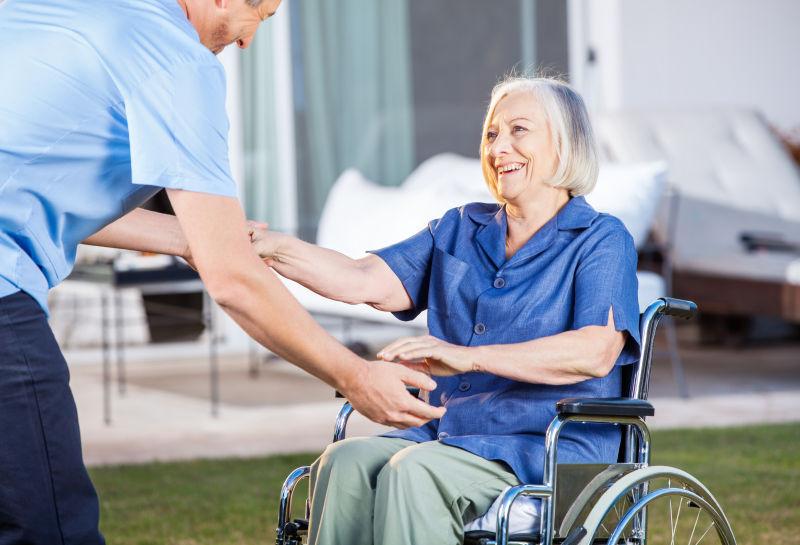 看护者帮助老妇人从轮椅上站起来