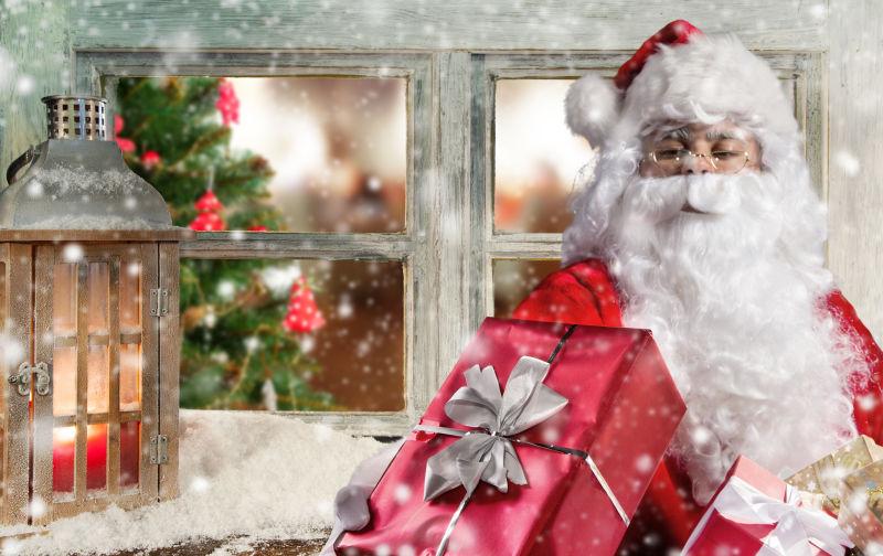 圣诞老人拿着圣诞礼物站在圣诞窗台装饰前