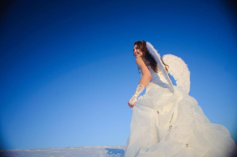 美丽的年轻天使穿着婚纱走在雪地上
