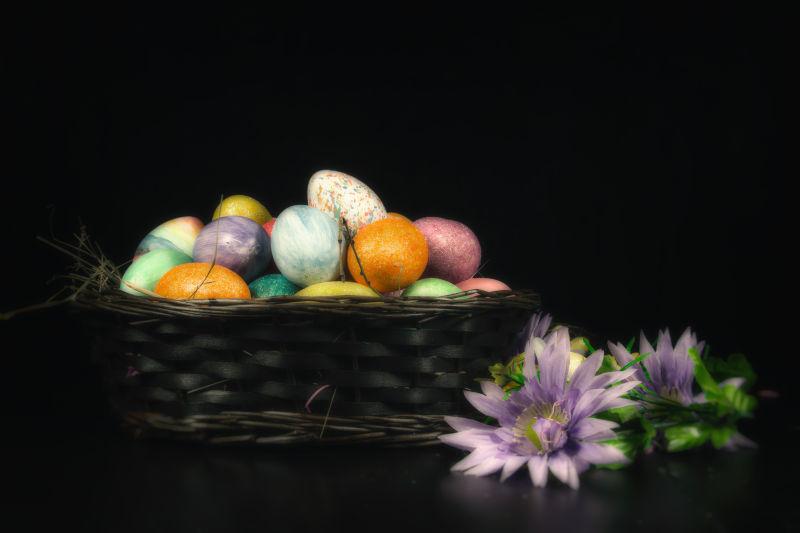 黑色背景上的篮子里的复活节彩蛋和紫色的花朵