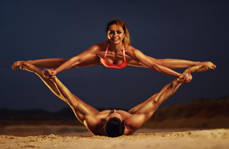 年轻的体育情侣在黄昏沙滩上做瑜伽练习
