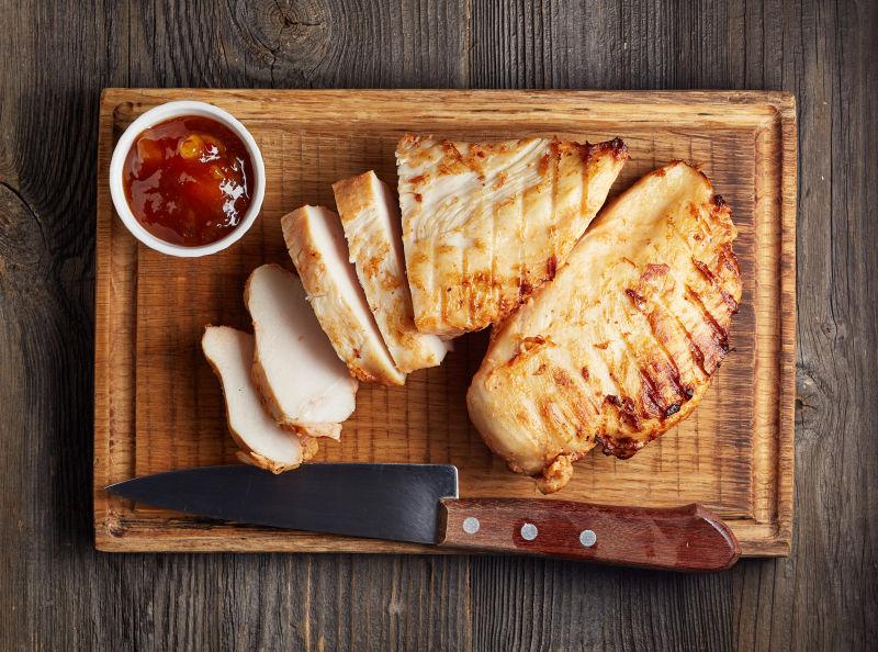 木制菜板上切片鸡胸肉刀具与蘸料