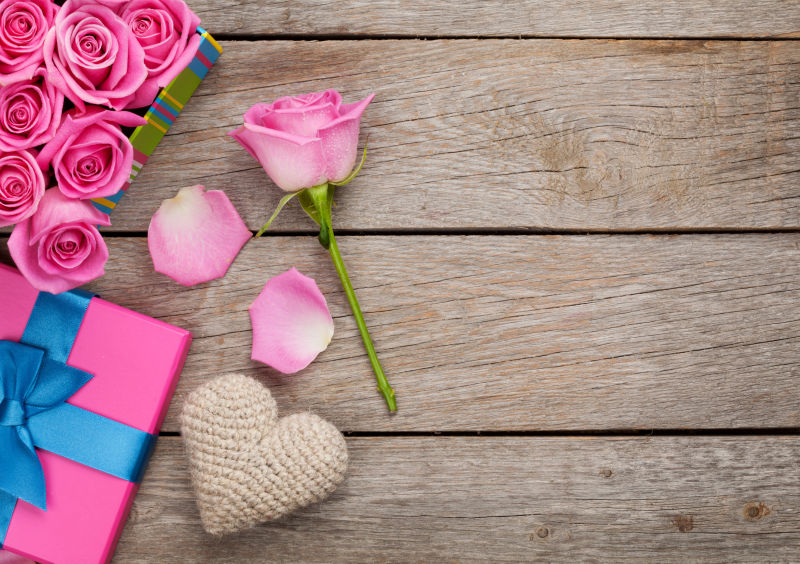 木制背景上的粉红色玫瑰和手工爱心饰品