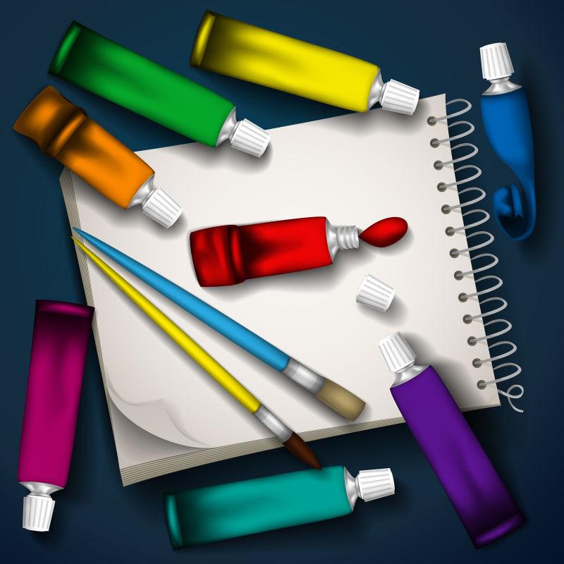 深色背景上的白色记事本上的彩色颜料管和画笔