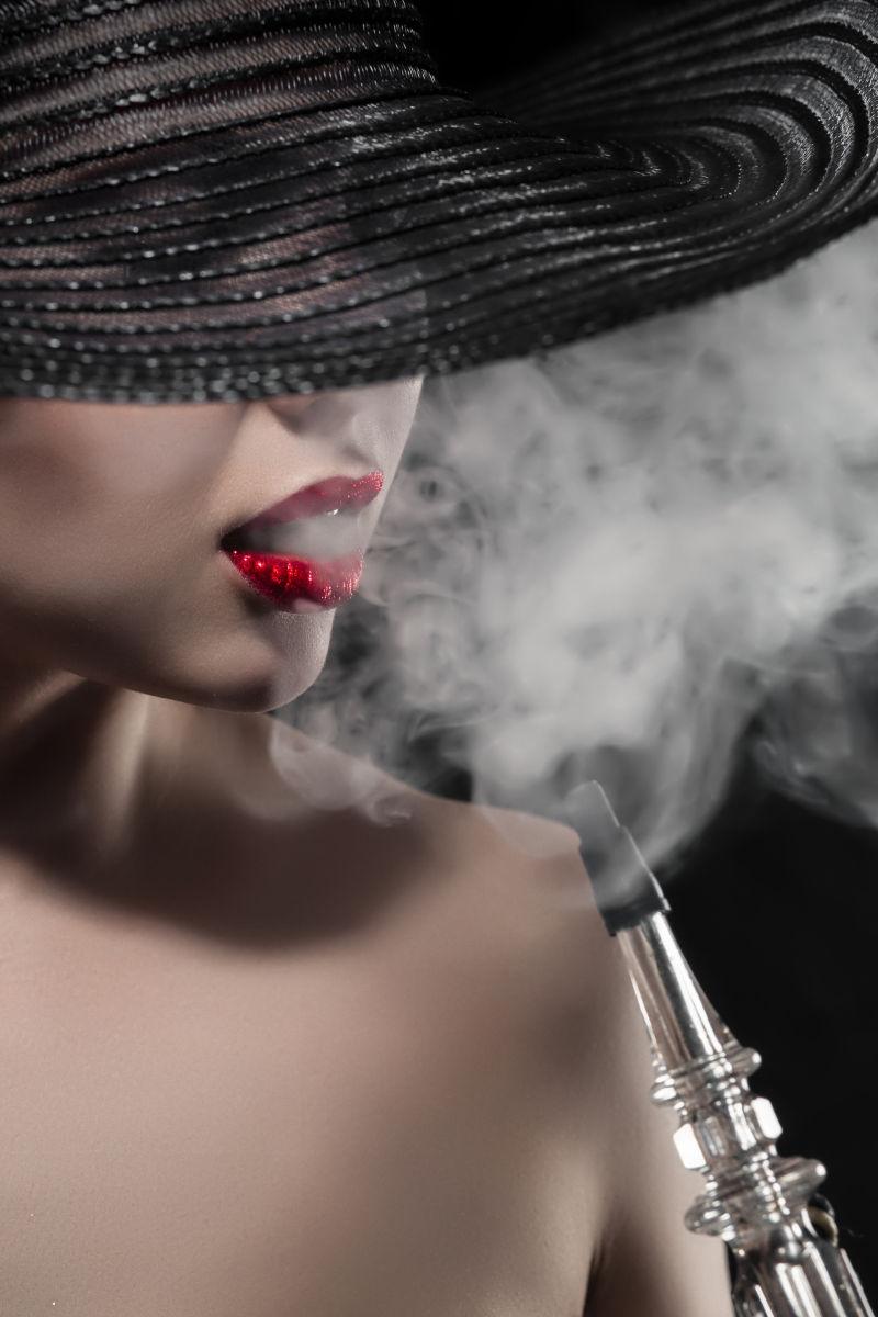 黑色背景中带着帽子吸水烟的美女