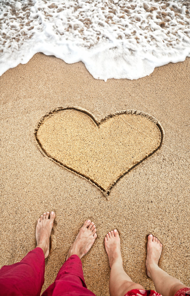 沙滩上的心形和年轻夫妇的脚