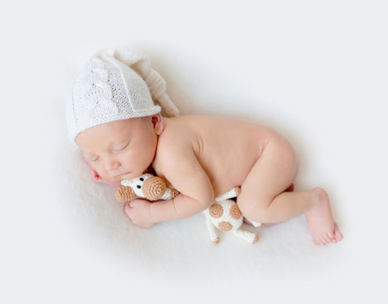 白色背景中带着编织帽子抱着玩具的新生儿