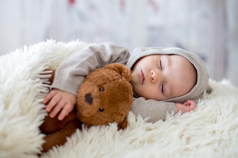 白色毛毯上抱着玩具熊睡觉的小婴儿