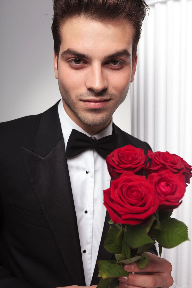 优雅的商人微笑着对着相机拿着一束红玫瑰