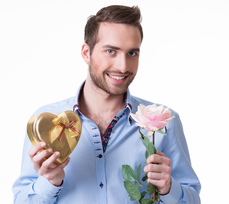 孤立的白色背景下拿着粉红色的玫瑰和礼物的年轻的快乐男子
